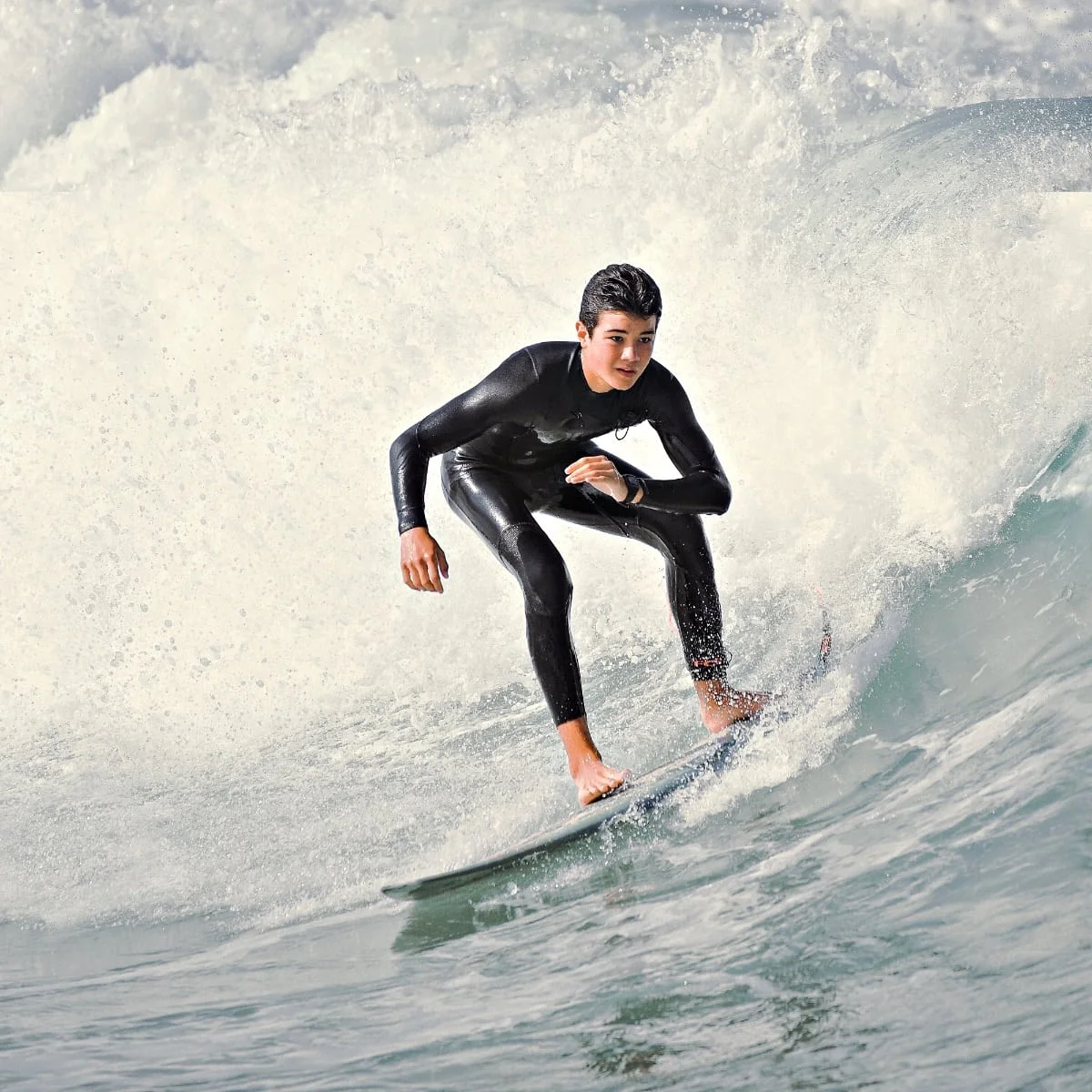 Un adolescent en combinaison noire surfe sur une grosse vague au cours d’un surfari.