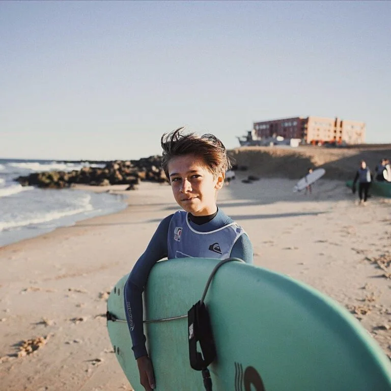 Un adolescent tient sa planche de surf sous le bras sur la plage.