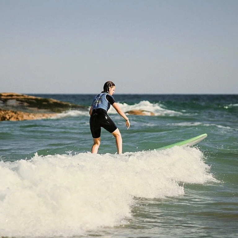 Une adolescente, de dos, surfe une belle vague pleine d'écume debout sur sa planche.