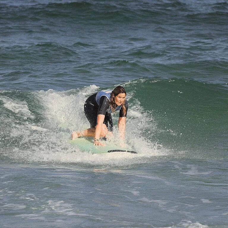 Une femme se relève sur sa planche de surf, poussée par une vague.