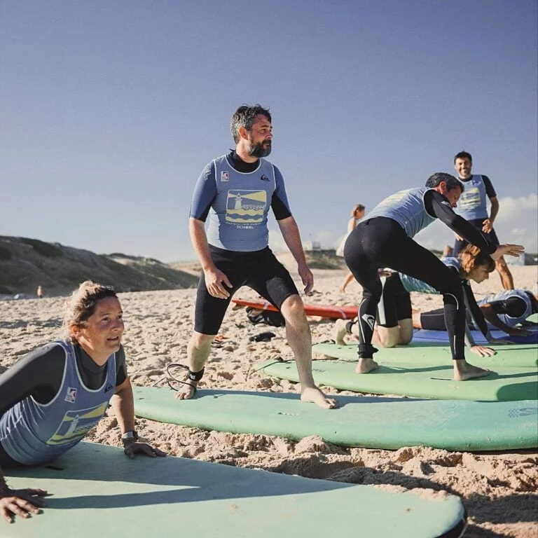 Un groupe d’adultes prennent un cours de surf et s’entraînent à se relever sur leurs planches de surf sur la plage avant d’aller à l’eau.