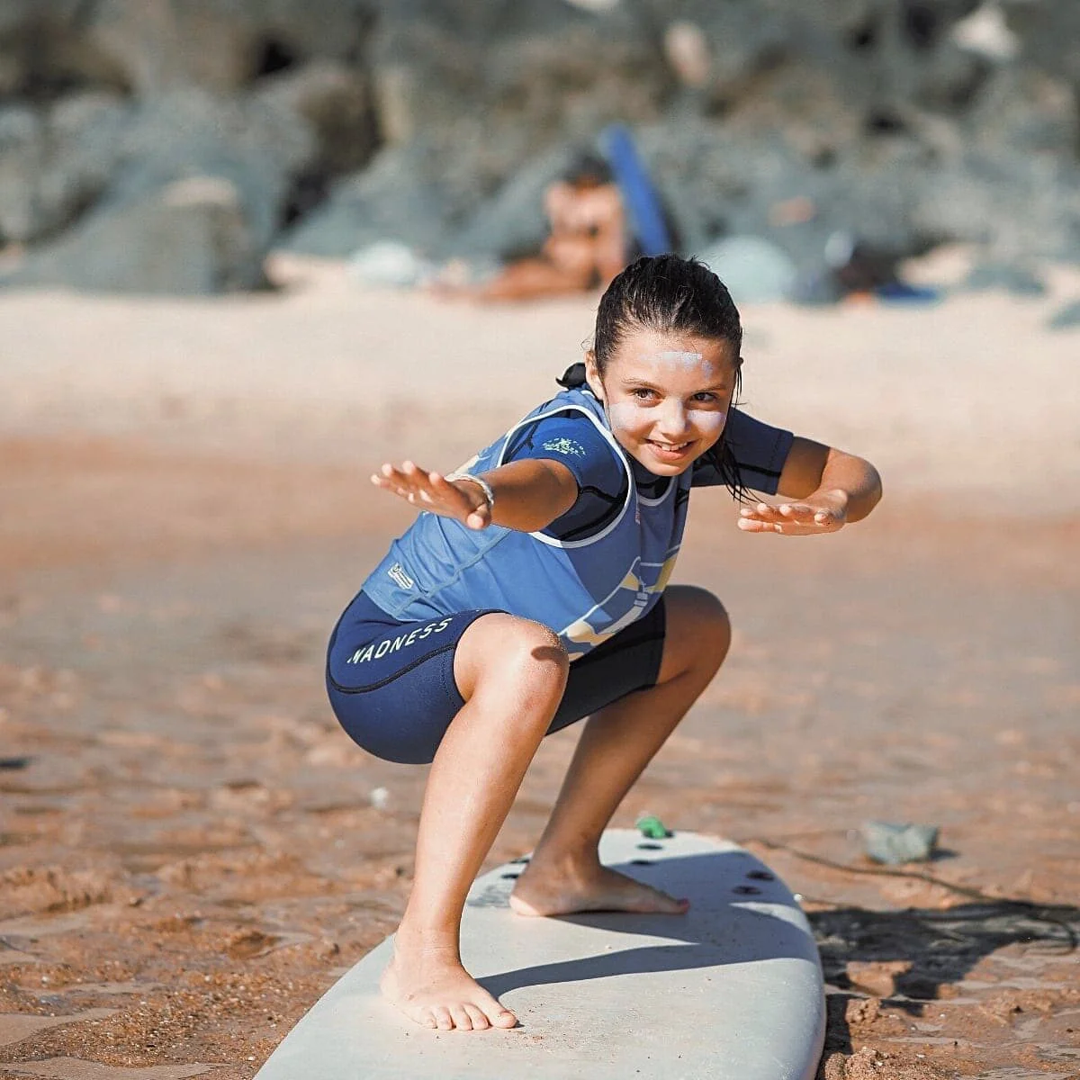 Une fillette s'entraine à tenir la position sur sa planche de surf, sur la plage.