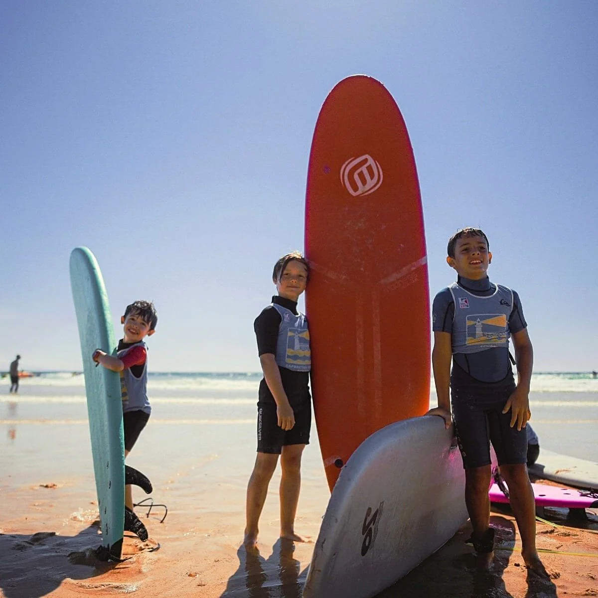 Un groupe d’enfants tient leur planche de surf debout sur la plage.