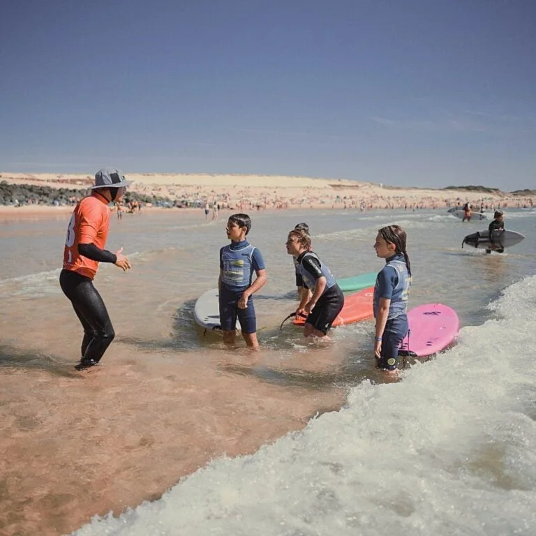 Un moniteur de surf donne des conseils à un groupe d’enfants, dans l’eau.