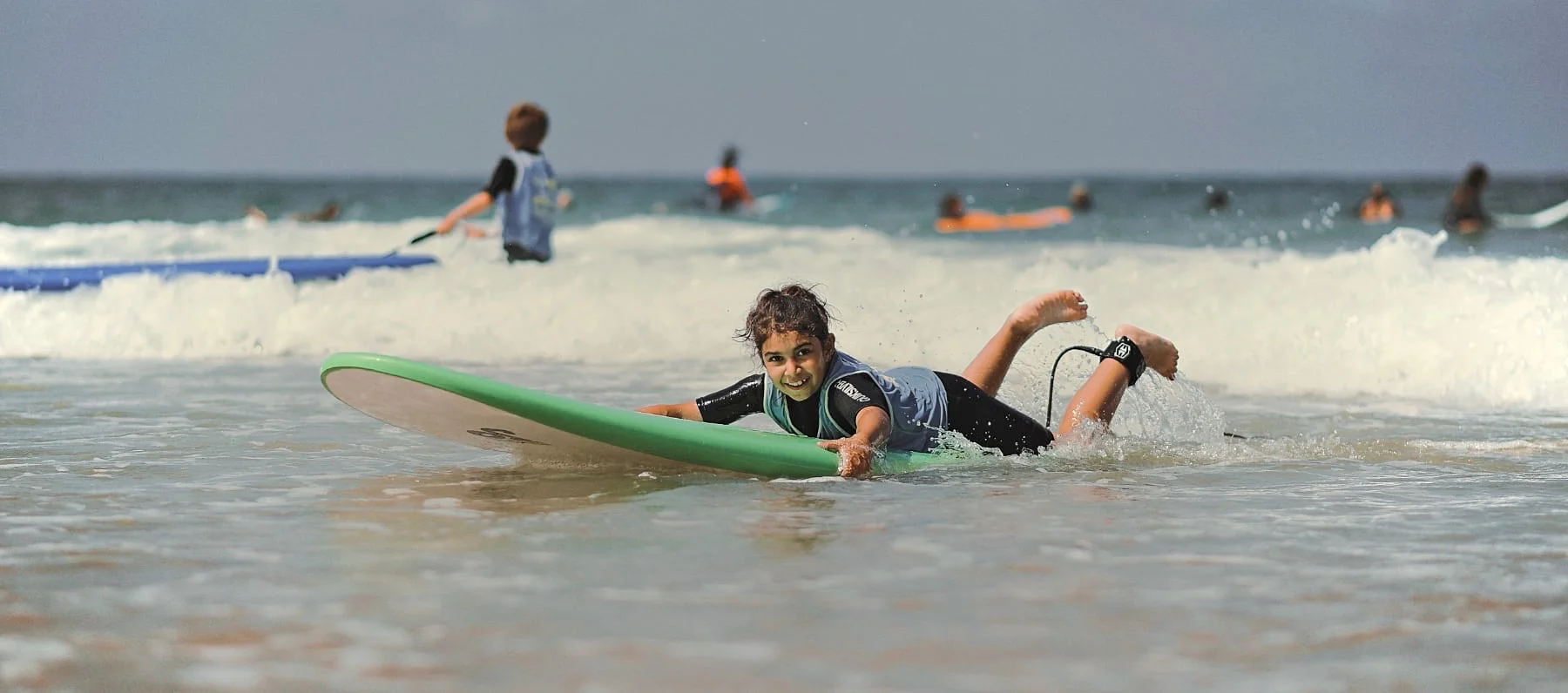 Une fille fait du surf allongée sur sa planche à Capbreton, et regarde en direction de la caméra.