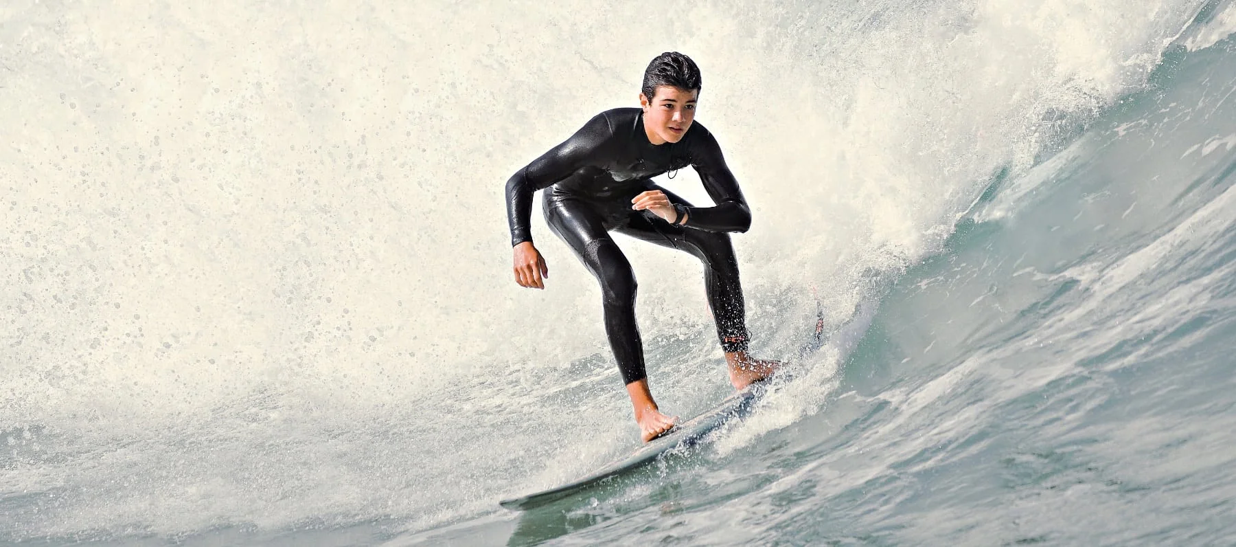 Un adolescent en combinaison noire surfe sur une grosse vague au cours d’un surfari.