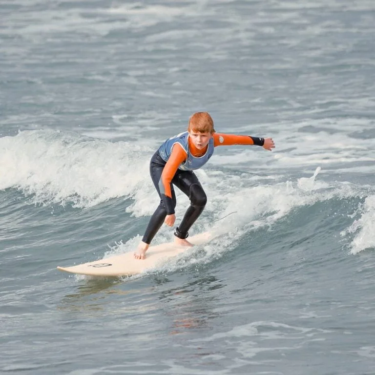 Un adolescent fait du surf debout sur sa planche, l’air concentré. Il est filmé au cours d’un coaching avec support vidéo.