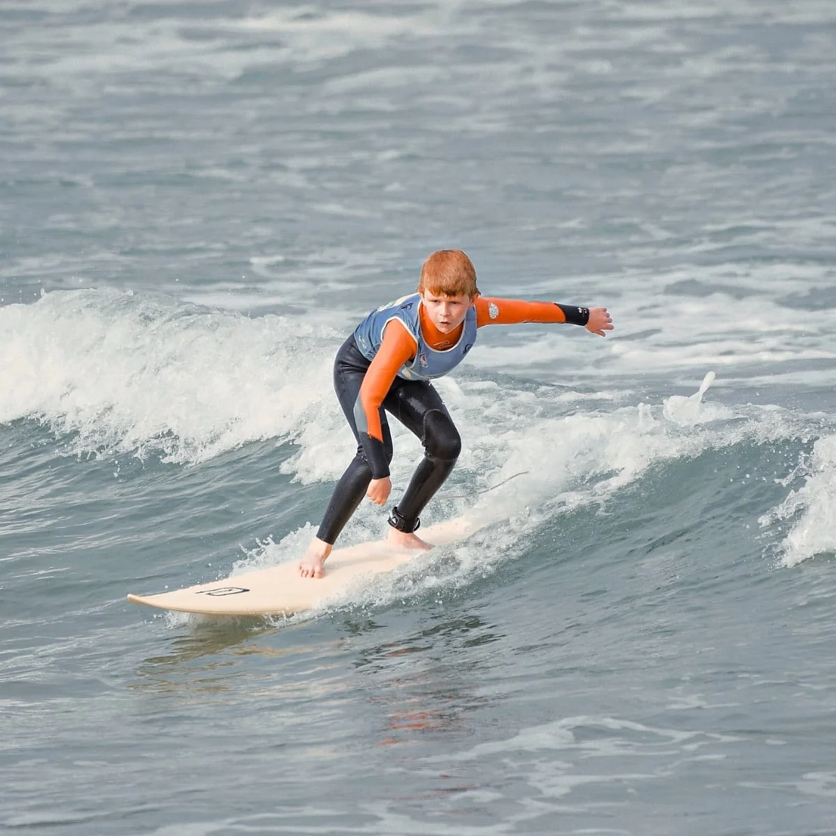 Un adolescent fait du surf debout sur sa planche, l’air concentré. Il est filmé au cours d’un coaching avec support vidéo.