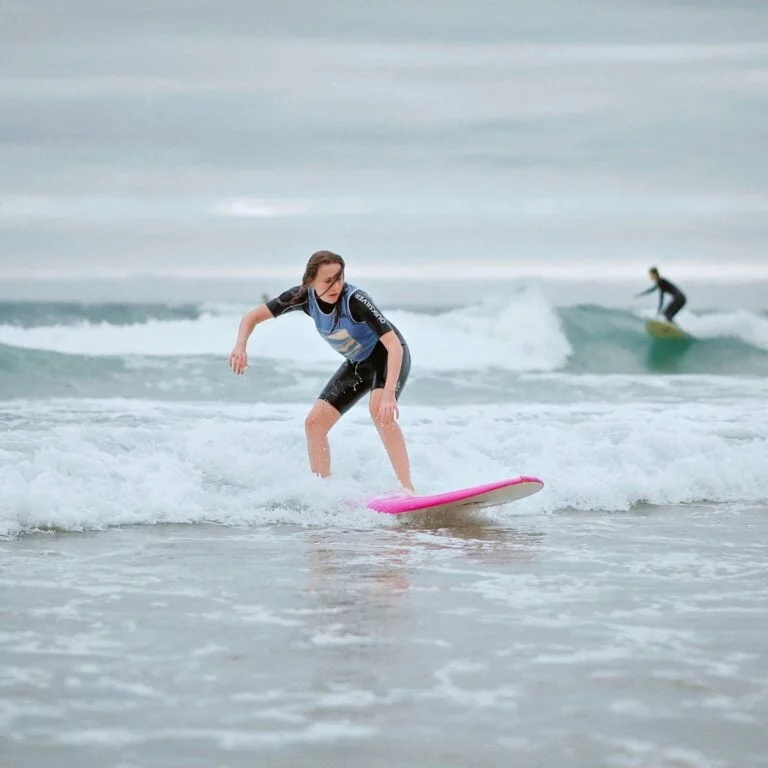 Une adolescente fait du surf debout sur sa planche. Elle a l’air à l’aise, et concentrée.
