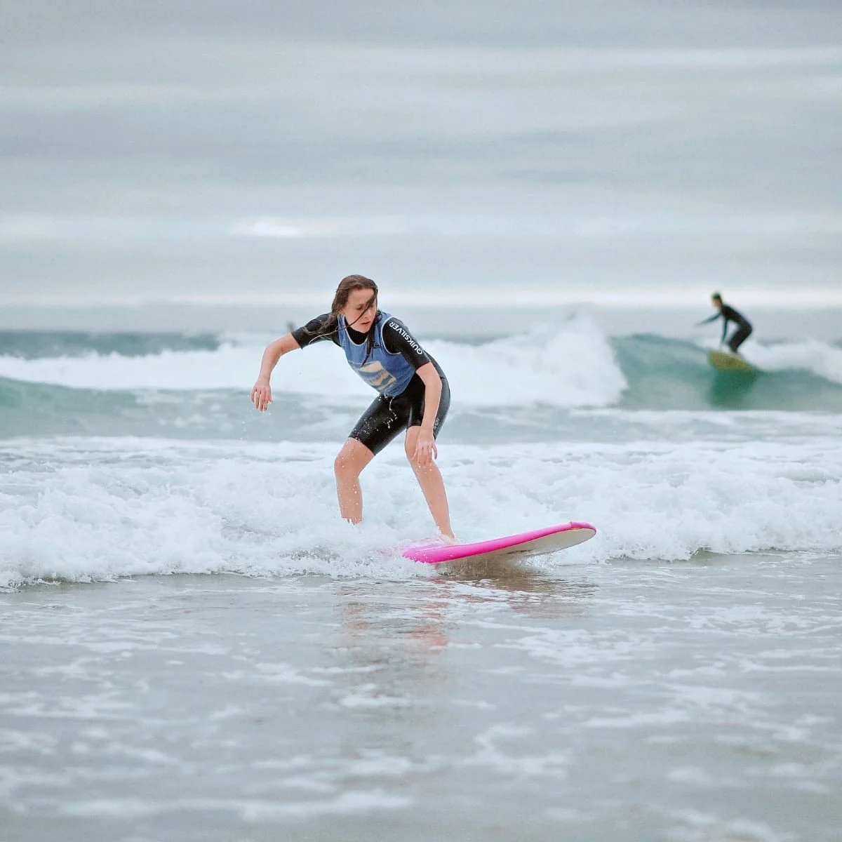 Une adolescente fait du surf debout sur sa planche. Elle a l’air à l’aise, et concentrée.