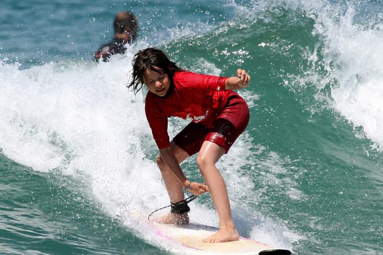 Un adolescent en combinaison de surf prend une vague, l’été, à Capbreton. Il fait beau et l’eau est claire.