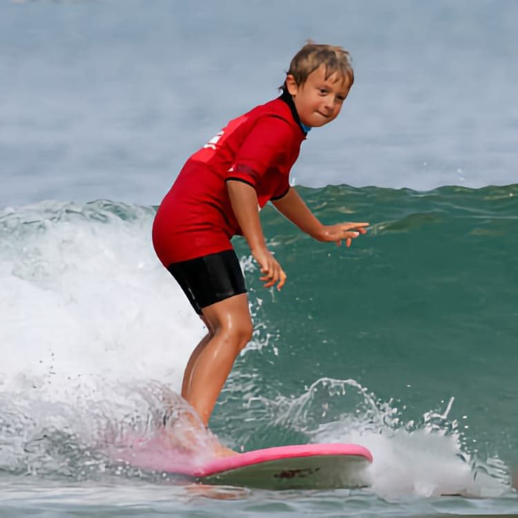 Un garçon combinaison de surf profite de l’été pour surfer sur une petite vague.